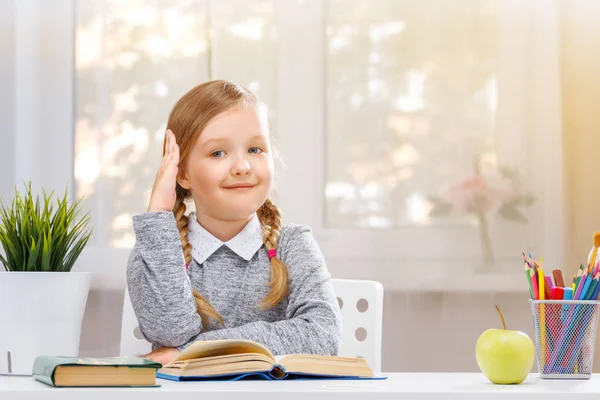 Piccola studentessa seduta al tavolo e tira su la mano. Il concetto di istruzione. Torniamo a scuola. Sfondo sfocato . — Foto Stock