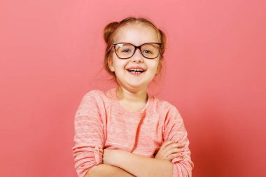 Güzel görünümlü sevimli sevimli neşeli neşeli içerik modern küçük çocuk kız pembe arka plan üzerinde gözlük kolları katlanmış Portre