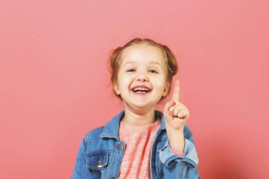 Komik küçük kız parmağını yukarı yaslar. Eğitim kavramı. Pembe arka plan.