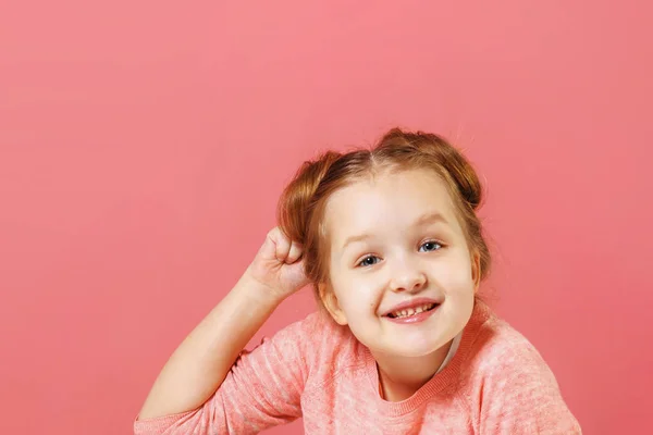Retrato de close-up de uma menina alegre com tufos de cabelo em um fundo rosa. A criança balança o punho . — Fotografia de Stock
