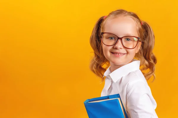 Pojęcie edukacji i szkoły. Wesoły dziewczynka uczeń w okularach posiadających książki na żółtym tle. Kopiuj przestrzeń. — Zdjęcie stockowe