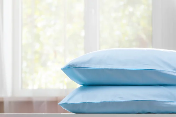 Крупный план двух голубых подушек лежит на комоде на фоне размытого окна. Копирование пространства . — стоковое фото