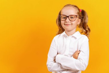Sarı renkli arka planda gözlüklü küçük bir kız. Çocuk kız öğrenci kollarını katlanmış ve kameraya güvenle bakar.