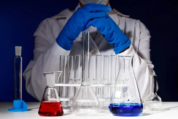W laboratorium chemii, Kobieta farmaceuta siedzi przy stole w otoczeniu probówek. Eksperyment medyczny. Chemik pracujący na teście z niebieskimi rękawicami. — Zdjęcie stockowe