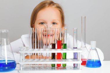 Küçük kız öğrenci test tüplerine bakıyor. Bir çocuk kimyasal bir deney yürütüyor..