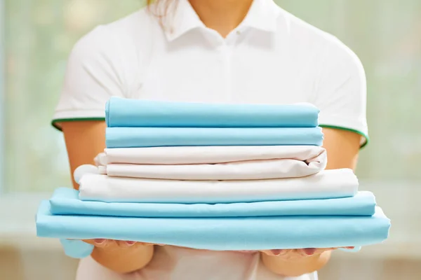 Closeup of woman\'s hand holding a stack of clean folded bed sheets of blue and white colors. Blurred background.