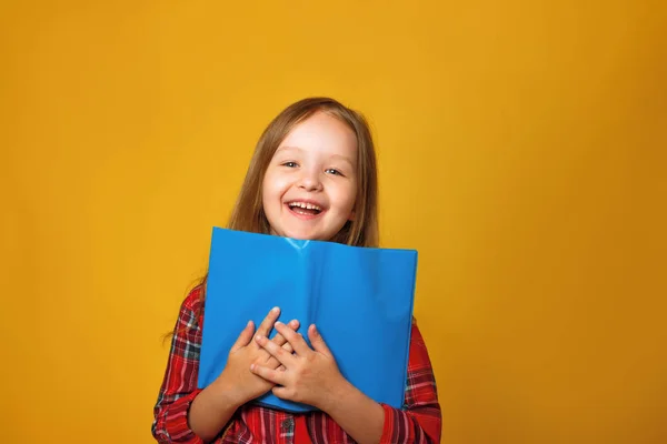 Sarı bir arka plan üzerinde neşeli küçük kız öğrenci. Çocuğun elinde açık bir kitap var. Eğitim ve okul konsepti.