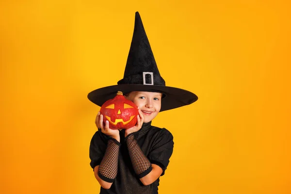 Cute little girl dressed in a witch costume holds a pumpkin jack lantern on a yellow background. Halloween celebration — Stock Photo, Image