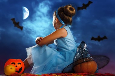 Cadılar Bayramı kutlaması. Prenses Külkedisi gibi giyinmiş küçük bir kız sırtı kabaklarla çevrili olarak oturur ve akşam ay ışığında gökyüzüne bakar..