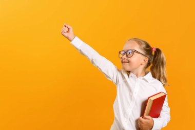 Başarı ve eğitim kavramı. Gözlüklü küçük bir kızın yakın arkadaşı ve sarı bir arka plan üzerine bir kitap. Çocuk kız öğrenci elini kaldırdı