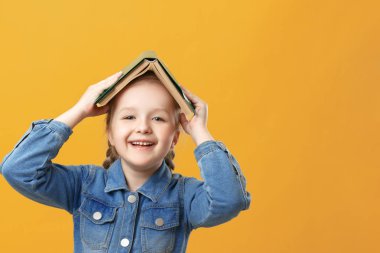 Sarı arka plandaki komik küçük bir kızın portresi. Öğrencinin kafasında bir kitap var..