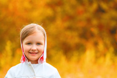 Sevimli sevimli gülümseyen küçük kız portresi sonbahar parkta ayakta, kameraya bakarak. Bulanık arka plan