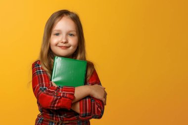 Sarı bir arka plan üzerinde kırmızı elbiseli sevimli bir küçük kız portresi. Çocuk kız öğrencinin elinde bir kitap var. Eğitim kavramı.
