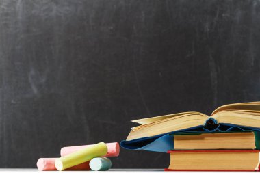 Tahta okulunun arka planında bir yığın kitap ve çok renkli tebeşir. Eğitim kavramı. Okula geri dön. Kopyalama alanı.