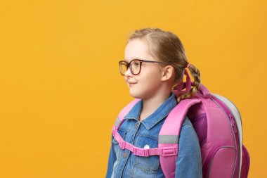 Sarı arka plan da profilinde sırt çantası olan küçük bir kız. Gözlüklü çocuk yakın çekim. Okula geri dön. Eğitim kavramı.