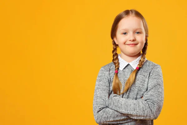 Portrét veselého děvčátku na žlutém pozadí. Dětská školka složila ruce a dívá se do kamery. — Stock fotografie