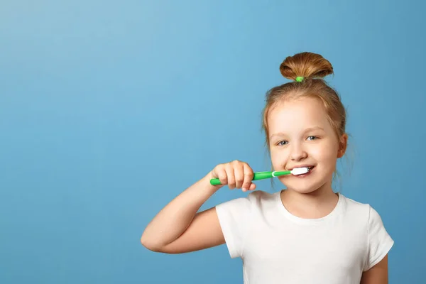 Je to portrét malé holčičky na modrém pozadí. Dítě si kartáčkem vyčistil zuby. Pojem každodenní hygieny. Kopírovat místo — Stock fotografie