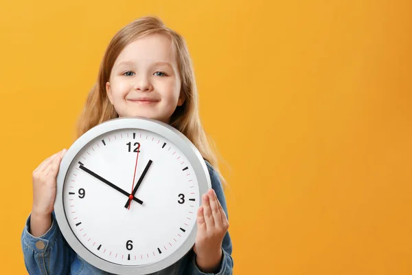 A cute little girl holding a big clock over a yellow background. The concept of education, school, timing, time to learn. Copy space.