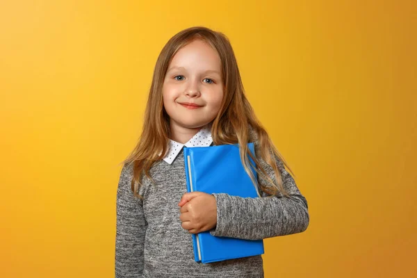 Close-up portret van kleine meisje schoolmeisje op gele achtergrond. Het kind houdt boeken. Het concept van onderwijs en school. Ruimte kopiëren — Stockfoto