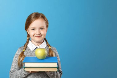 Mavi arka plan üzerinde neşeli bir küçük kız portresi. Liseli kız elinde bir yığın kitap ve bir elma tutuyor. Okula geri dön. Eğitim kavramı.
