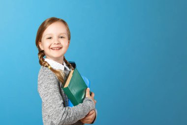 Mavi arka plandaki küçük bir kız öğrencinin yakın çekim portresi. Çocuğun elinde kitap var. Eğitim ve okul kavramı. Kopyalama alanı