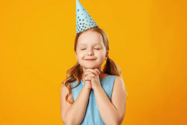 Cute little girl celebrates birthday. The child closed his eyes and made a wish. Closeup portrait on yellow background. — Stock Photo, Image