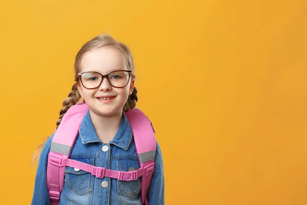 Portret van een klein meisje schoolmeisje met een rugzak op een gele achtergrond. Kind met glazen close-up. Terug naar school. Het begrip onderwijs. — Stockfoto