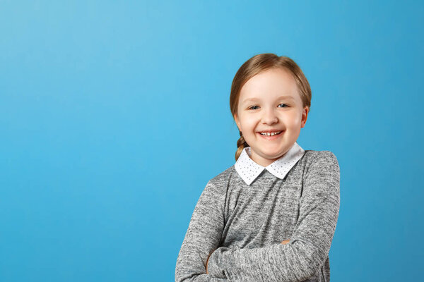 Portrait of a cheerful little girl on a blue background. Child schoolgirl laughs and looks into the camera. Copy space