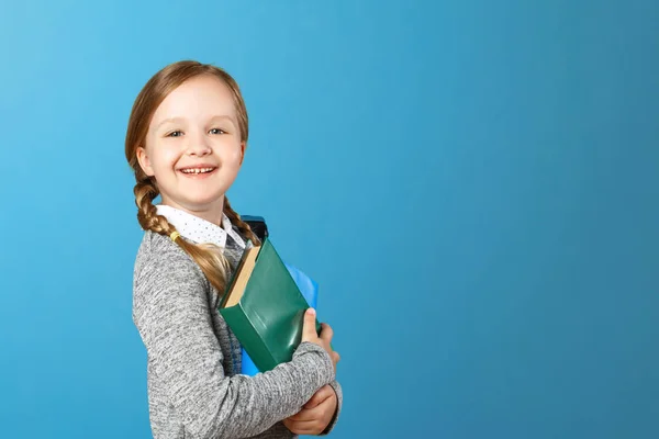 Close-up portret van een klein meisje schoolmeisje op een blauwe achtergrond. Het kind houdt boeken. Het concept van onderwijs en school. Ruimte kopiëren — Stockfoto