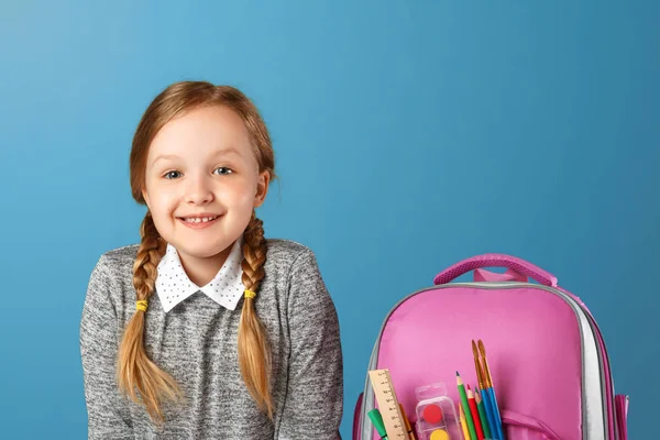 Close-up portret van kleine meisje schoolmeisje met rugzak op blauwe achtergrond. Terug naar school. Het begrip onderwijs. — Stockfoto