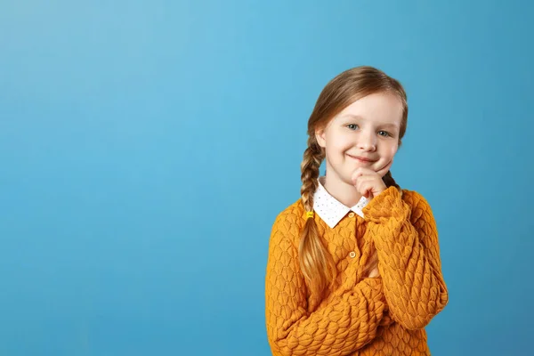 Portrét malé dívčí dívky ve žlutém svetru na modrém pozadí. Odporné dítě držící ruku na bradě a dívá se na kameru. Kopírovat místo — Stock fotografie