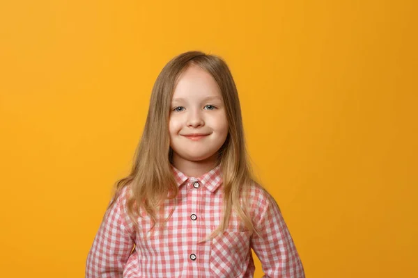 Portrét té zábavné malé blondýny na žlutém pozadí. Dítě v růžové košili se dívá do kamery. — Stock fotografie