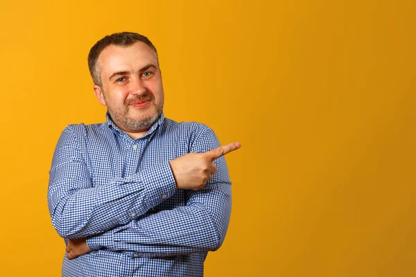 Bir gömlek yakışıklı sakallı adam, yan parmağını işaret, kameraya bakar ve gülümser, sarı bir arka plan karşı. Kopya alanı. Close.