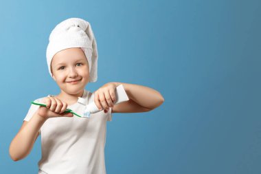 Mavi arka plandaki küçük bir kızın yakın çekim portresi. Çocuk dişlerini fırçalar ve diş fırçasının üzerine diş macunu sıkıyor. Günlük hijyen kavramı. Kopyalama alanı.