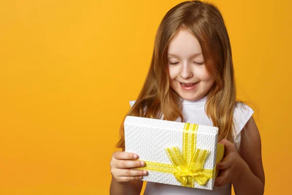 Ritratto di una bambina felice che apre una scatola regalo con un regalo su sfondo giallo — Foto Stock