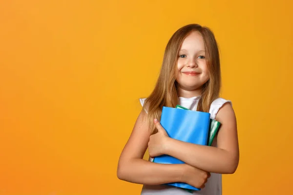 Primo piano ritratto di bambina scolara su sfondo giallo. Il bambino tiene dei libri. Il concetto di istruzione e scuola. Copia spazio — Foto Stock