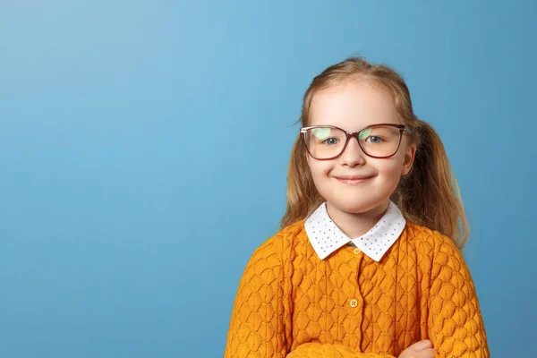 Portrét holčičky s brýlemi. Hezké dítě ve žlutém svetru na modrém pozadí. Kopírovat místo — Stock fotografie