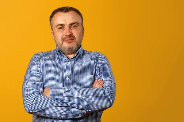 Serious man with folded arms and a deadpan expression posing in front of a yellow background. Copy space