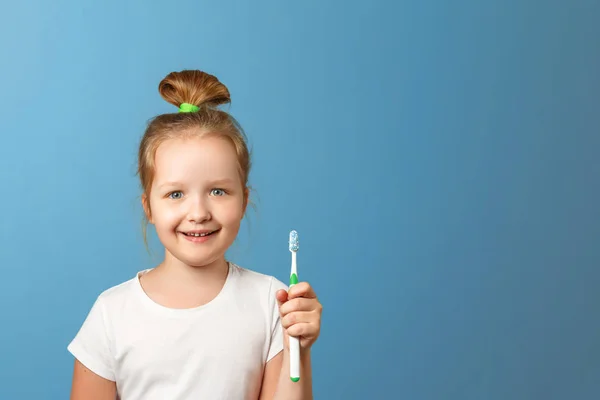 Je to portrét malé holčičky na modrém pozadí. Dítě má zubní kartáček. Pojem každodenní hygieny. Kopírovat místo. — Stock fotografie