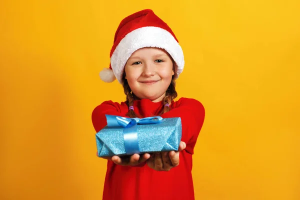 Ragazzina felice con regalo di Natale. Un bambino con un cappello da Babbo Natale fa un regalo — Foto Stock