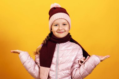 Sarı bir arka plan üzerinde bir ceket, eşarp ve şapka büyüleyici sevimli küçük kız Portresi. Sonbahar ve kış konsepti