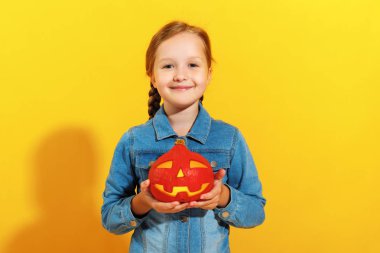 Bir kot gömlek neşeli küçük kız sarı bir arka plan üzerinde bir kabak jack fener tutar. Cadılar Bayramı kutlaması