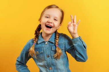 Sarı arka plan üzerinde kot gömlekli küçük bir kız. Çocuk Bir Ok işareti gösterir. Başarı kavramı, onay