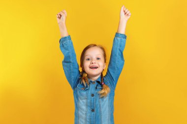 Neşeli mutlu küçük kız ellerini kaldırdı. Sarı arka plan üzerinde kot gömlekli bir çocuk