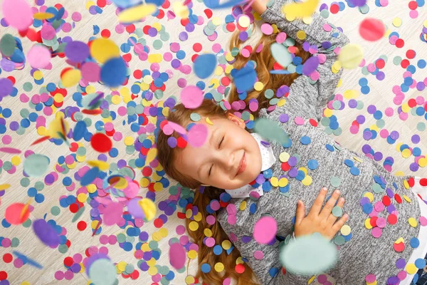 Little girl lying on the floor under falling confetti — Stock Photo, Image