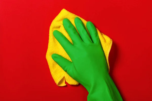 Ręka w zielonej rękawicy ochronnej z żółtą serwetką na czerwonym tle. Koncepcja sprzątania, opieki domowej — Zdjęcie stockowe