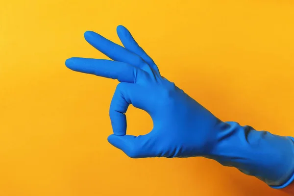 Ręka w niebieskiej rękawicy ochronnej na żółtym tle. Palce pokazujące znak Ok — Zdjęcie stockowe