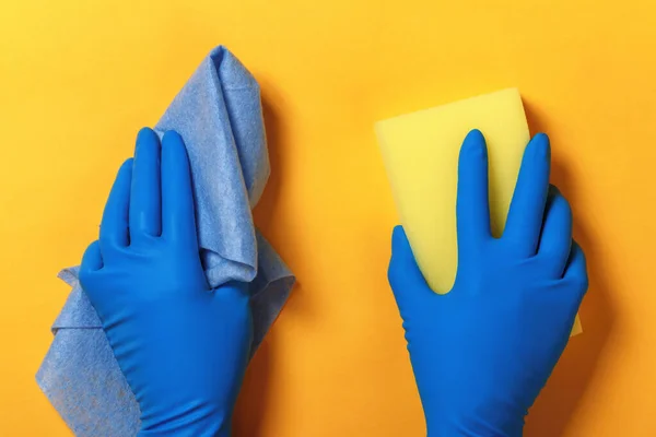 Hände in blauen Schutzhandschuhen halten einen Schwamm und eine Serviette auf gelbem Hintergrund — Stockfoto