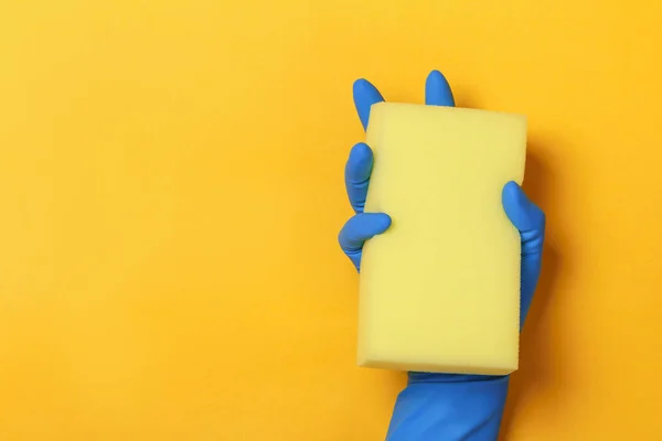 Koruyucu mavi eldivenli bir el sarı renkli bir arka planda sünger tutar. — Stok fotoğraf