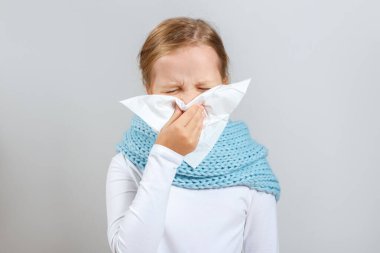 Soğuk mevsim. Sıcak eşarplı küçük kız burnunu siliyor. Gri arka planda bir çocuk